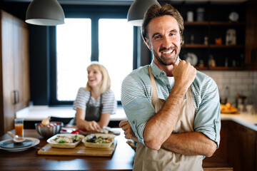 Beautiful young couple is smiling while cooking together in kitchen at home