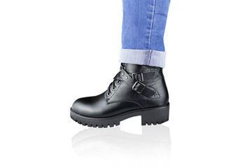Leg in blue rolled up jeans and black lace-up boot with buckles and straps, isolated on white.