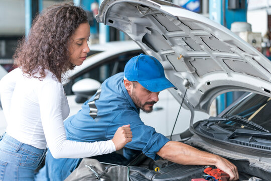 Auto services and Small business concepts. Mechanic reparing the car in the workshop garage. The technician is explaining the customer about the breakdown of the vehicle.