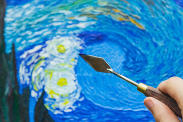 the hand of a European artist holds a mastekhin smeared in oil paint on the background of a painted picture. Van Gogh's replica Moonlit Night