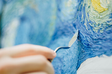 the hand of a European artist holds a mastekhin smeared in oil paint and draws a picture. Van Gogh's replica Starry night. blurred background. Close-up