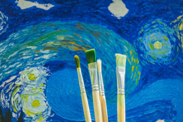 paint brushes smeared in oil paint and draws a picture. Van Gogh's replica Starry night. blurred background. Close-up
