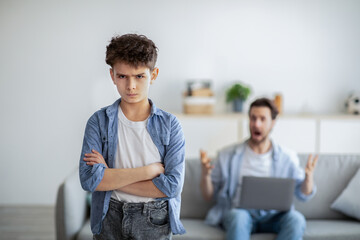 Family problems during quarantine. Angry father shouting at son while sitting with laptop computer on sofa at home