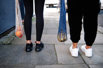 Anonymous girlfriends with eco friendly bags walking on street