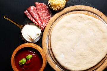 Food concept homemade pizza dough and pizza ingredients on wooden board on black background with copy space
