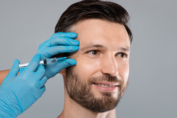 Closeup of happy handsome bearded man getting under eye injection