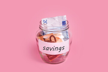 Euro banknotes in glass money jar with savings label, financial, saving. Money box with word SAVINGS on sticky note paper. Jar full of cash, save money concept, expense planning and control.