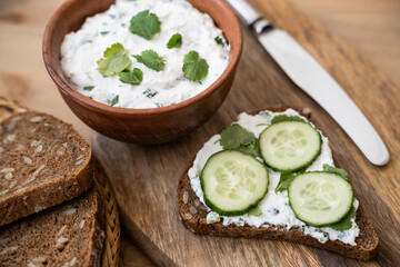 Cereal bread with curd cheese, cucumber and herbs on a wooden background. Delicious and healthy food, vegetarian breakfast. Close-up.