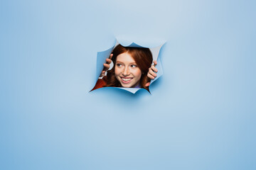 happy redhead young woman looking away on blue ripped background.