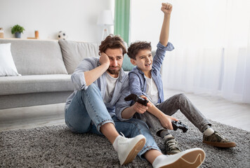 Video gamers. Joyful boy winning dad in online game, celebrating victory and raising hand