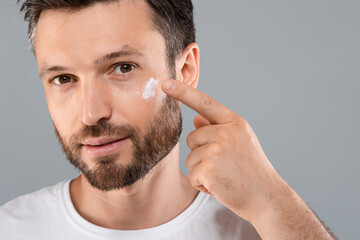 Obraz premium Closeup of bearded man applying face cream on grey