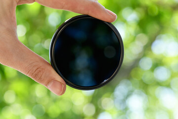 Hand hold  ND filter (neutral density) against blue sky. Light background.