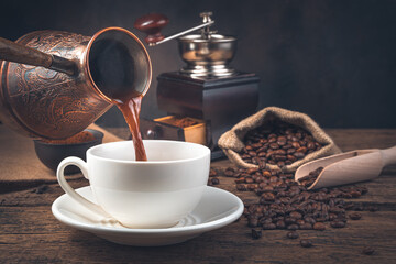 The process of pouring coffee into a mug of Turki on the background of a coffee grinder and coffee beans.