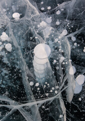 Frozen Baikal lake with cracks and methane bubbles on the transparent ice surface. Winter abstract and blue ice background.