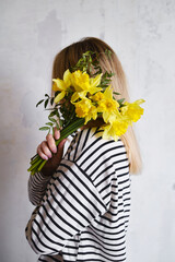 Yellow daffodils in the hands of a happy woman. Stylish daffodils in the hand of the florist. A girl in a striped sweater gathered a fresh bouquet. Beautiful spring delicate flowers. Holiday gift