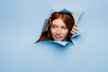 amazed redhead young woman looking away on blue ripped background.