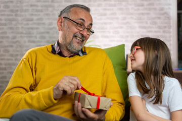 Obraz premium Happy family aged man and girl smiling and opening gift box while resting on sofa during holiday celebration at home. 
