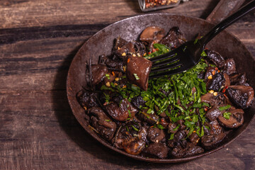 Fried royal champignons in an old cast-iron skillet with trendy hard light, dark shadow