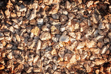Background or backdrop made of small pieces of brown pebbles or break stones at a bright sunny day lit with warm sunlight. Vacation or travelling concept. Horizontal orientation image