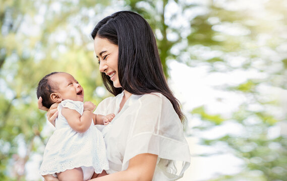 Close up portrait of beautiful young asian mother laught her newborn baby at spring outdoor park. Healthcare medical love caucasian woman lifestyle mother's day breastfeeding concept copy space.