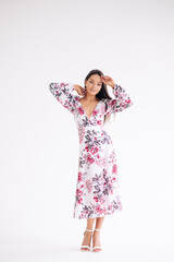 Young woman stands dressed in floral pattern dress on white background.
