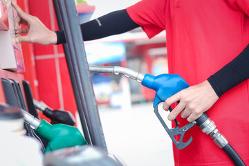 Gas station attendant in red uniform holding a fuel petrol pump nozzle against at gas station.