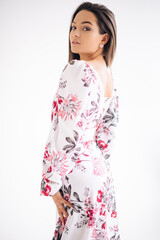 Young woman stands dressed in floral pattern dress on white background.