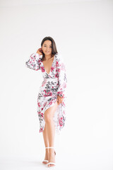 Young woman stands dressed in floral pattern dress on white background.