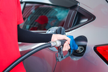Hand of gas station attendant holding a fuel petrol pump nozzle against for filling up the car with petrol at gas station.