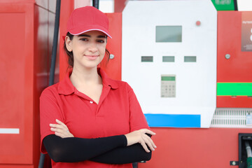 Portrait of happy smiling beautiful woman gas station attendant in red uniform standing with crossed arms at gas station.