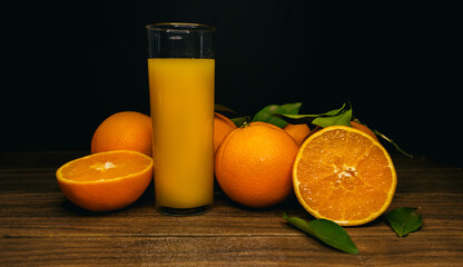 A glass of orange juice and slices of orange on a wooden board on a black background