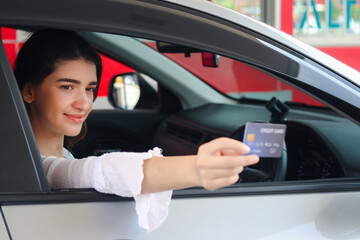 Fototapeta na wymiar Customer woman holding credit card (mock up) for payment at gas station, young beautiful lady in car waiting for to pay with credit card.