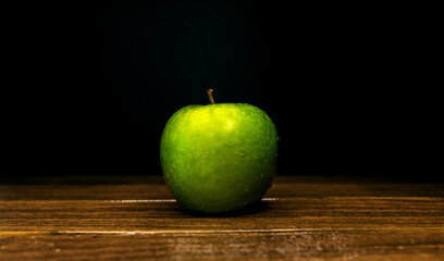 green apple with water drops on a wooden board on a black background