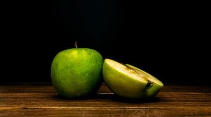 green apple slice with water drops on a wooden board on a black background