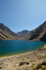 The deep blue color water lake very high in the Andes mountains. View of the Inca Lagoon in Chile, surrounded by rocky mountains and cliffs.