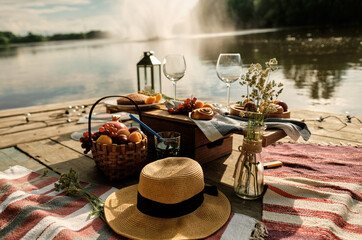 Romantic picnic by the river with panoramic backdrop. The beauty of the setting sun, fresh fruits, pastries and wine. A romantic outdoor dinner.