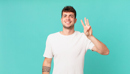 handsome man smiling and looking friendly, showing number three or third with hand forward,...