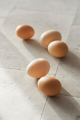 Raw chicken eggs background on white textured table with sunny light. Close up view, selective focus, copy space. Organic, healthy eating, keto diet concept.