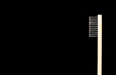 Eco-friendly antibacterial bamboo wood toothbrush with white bristles on a black background.