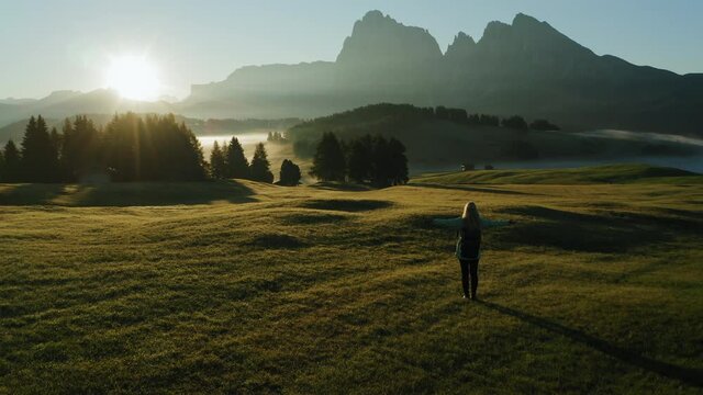 Alpe di Suisi, Dolomites. Girl silhouette at sunrise with raised hands. Aerial drone view of Alpine meadow mountain Plateau in Italy. Idyllic Seiser Alm valley in South Tyrol. Europe