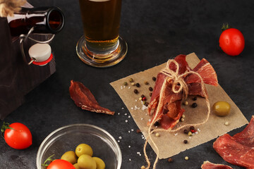 Natural snack for beer. Pieces of spicy jerky tied with twine on parchment paper against a dark...