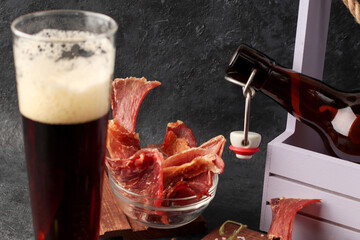 Natural snack for beer. Organic homemade food. Pieces of jerky with spices in a glass cup on a dark background. Condiments and coarse salt, cherry tomatoes, olives. Natural snack for beer. Close-up
