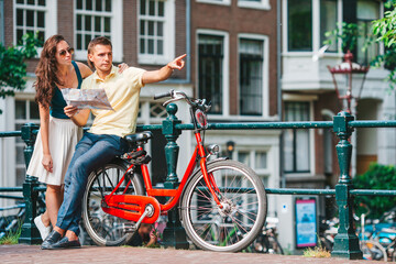Plakat Young happy caucasian couple on bikes in old streets in Amsterdam