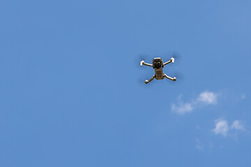 White unmanned aerial vehicle with four propellers and blades is on the blue sky background