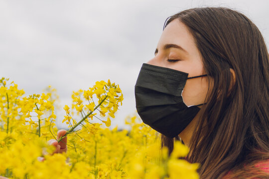 Girl In A Field With Mask Smelling The Yellow Flowers