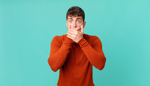 handsome man covering mouth with hands with a shocked, surprised expression, keeping a secret or saying oops