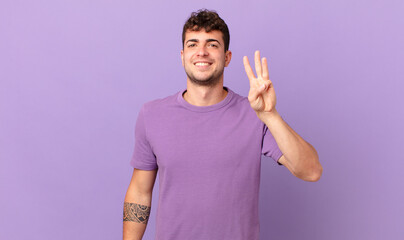handsome man smiling and looking friendly, showing number three or third with hand forward,...