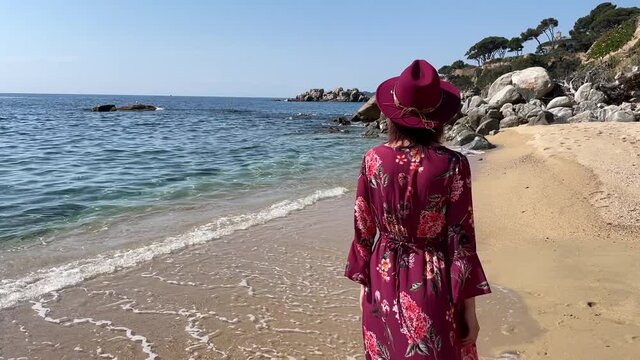 an elegant woman with purple dress and hat walking at the beach in her holidays
