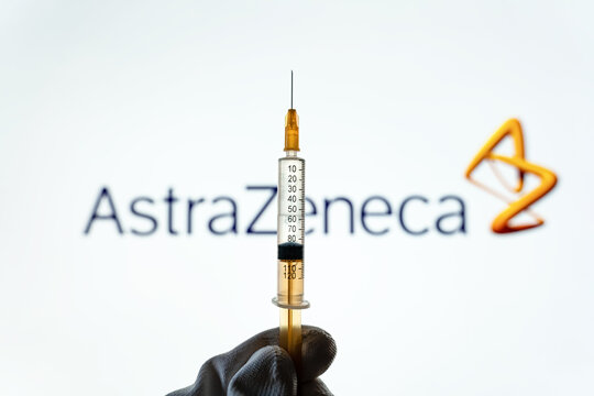 Kyiv, Ukraine &ndash; April 18, 2021: Hand of medical worker in surgical glove holds syringe against AstraZeneca Logo, selective focus. Vaccination of the population.