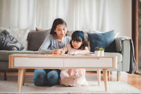 Happy Asian family mother and daughter study or drawing together at home in living room